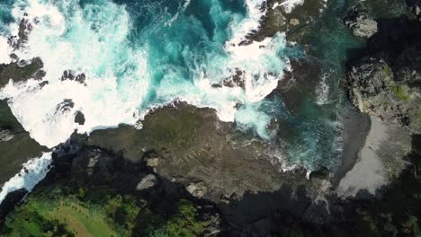 Aerial-top-down-of-massive-waves-crashing-against-rocky-coastline-and-beach