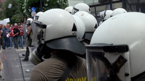 Greek-riot-police-carrying-shields,-wear-helmets-and-gas-masks-come-under-attack-from-missiles-during-a-public-order-event
