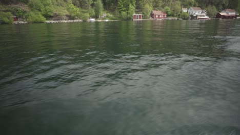 Punto-De-Vista-De-Un-Velero-En-Un-Lago-Tranquilo-Con-Casas-Tradicionales-De-Madera-Junto-A-La-Orilla-En-Noruega