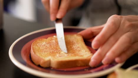Spreading-butter-with-a-kitchen-knife-on-a-toast-sliced-bread-on-a-plate-close-up-shot
