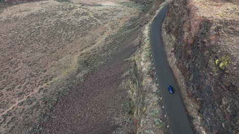 Aerial-of-a-blue-SUV-driving-along-a-cliff-in-Washington's-desert-region