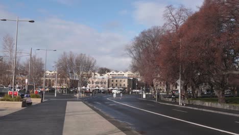 Looking-down-wet-road-towards-Salamanca-Place-on-clear-winter-day-as-car-drives-down-road,-Hobart,-Tasmania,-Australia