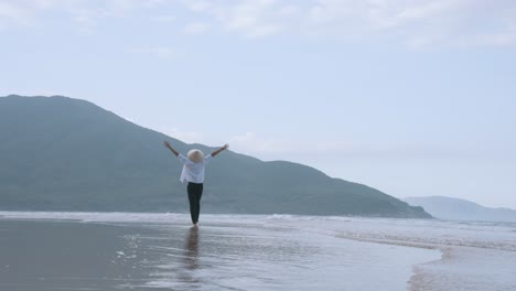 Un-Hombre-Que-Se-Siente-Agradable-Caminando-Hacia-La-Montaña-En-La-Playa-Con-Un-Sombrero-Cónico-De-Hoja-De-Palma-Vietnamita