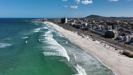 Drone-flight-over-Bloubergstrand-shoreline-with-beachfront-buildings-in-Cape-Town,-South-Africa,-at-sunny-day