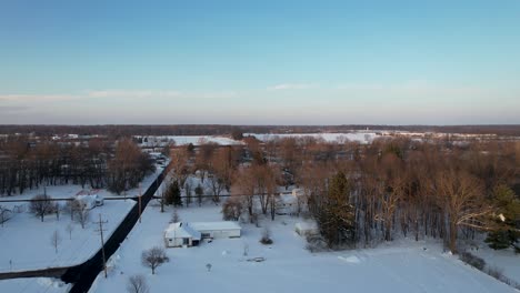 An-aerial-view-of-a-field-covered-with-snow,-rural-road,-blue-sky-and-trees-covered-by-frost