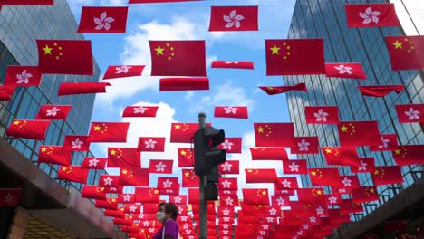 Menschen-überqueren-Die-Straße,-Während-In-Hongkong-Flaggen-Der-Volksrepublik-China-Und-Der-SAR-Hongkong-Vor-Dem-1.-Juli,-Dem-Jahrestag-Der-Übergabe-Hongkongs-An-China,-Gezeigt-Werden