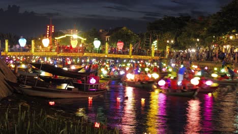 Timelapse-Hoi-An-Festival-De-Linternas,-Coloridas-Noches-Iluminadas-Con-Linternas,-Mucho-Tráfico-De-Botes-Y-Canoas-En-El-Río-Del-Canal-Y-Multitud-De-Turistas,-Navegación-Flotante-Bajo-El-Puente,-Linternas-Brillantes-A-Bordo