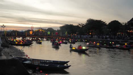 Laternenfest-Hoi-An-Vietnam,-Zeitraffer-Abendsonnenuntergangsansicht-Von-Beleuchteten-Booten,-Kanuverkehr-Auf-Dem-Flusskanal,-Unterquerung-Der-Brücke,-Touristen-An-Bord,-Besuchermenge-Im-Hintergrund