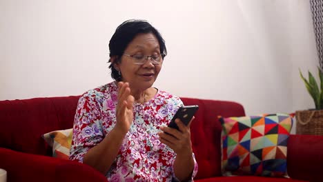 Ältere-Asiatische-Frau,-Die-Zu-Hause-Auf-Dem-Sofa-über-Einen-Handy-Videoanruf-Spricht