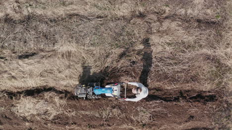 AERIAL---Man-working-a-field-with-a-rototiller,-agriculture,-wide-shot-pan-left
