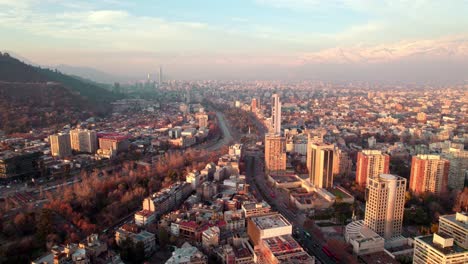 Aerial-dolly-in-of-traffic-in-Alameda-avenue,-Downtown-Santiago-city-buildings-and-mountains-in-background-at-sunset,-Chile