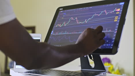 Man-swiping-stock-charts-while-day-trading-on-his-touchscreen-computer-at-his-home-office-area-working-from-home