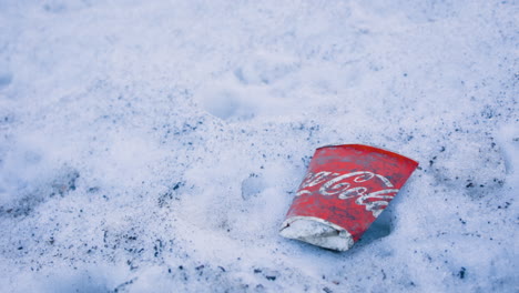 Cerrar-Toma-Panorámica-Lenta-De-Una-Taza-De-Coca-cola-De-Papel-Plana-En-La-Nieve-En-El-Suelo