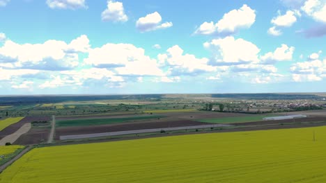Picturesque-View-Of-A-Countryside-With-Village-And-Canola-Farmland-Against-Blue-Cloudy-Sky