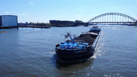 La-Primavera-Coal-Barge-Sailing-At-Noord-River-With-Arch-Bridge-In-Background-At-Hendrik-Ido-Ambacht,-Netherlands