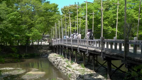 People-enjoying-the-view-from-Old-Wooden-Bridge-With-Green-Trees-In-Background-At-Korean-Folk-Village-In-Yongin-City,-Seoul,-South-Korea