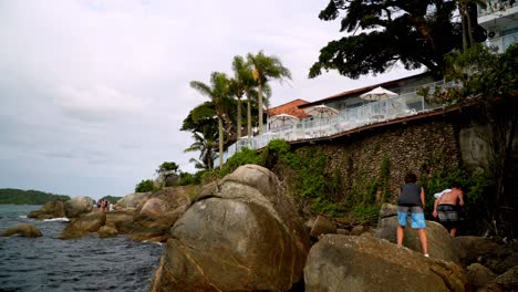 People-walking-through-big-stones-in-rocky-seashore-near-Bombas-and-Bombinhas-beach-Resort,-Brazil