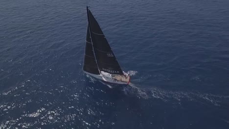 Aerial-circling-over-sailing-boat-with-black-sails-in-open-sea