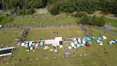 Drone-shot-of-people-standing-around-grass-playground-of-a-Dog-frisbee-event-in-Poznan-on-a-big-green-field
