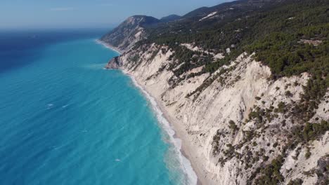 High-altitude-orbit-aerial-shot-of-blue-waves-hitting-the-coastline-of-Egremni-beach-in-Lefkada,-Greece