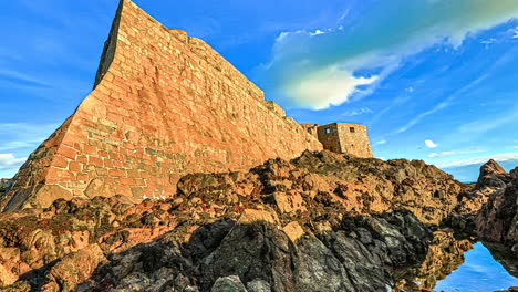 Time-lapse-shot-of-flying-clouds-at-blue-sky-and-lighting-old-brick-ruin-at-sea-shore-of-Guernsey