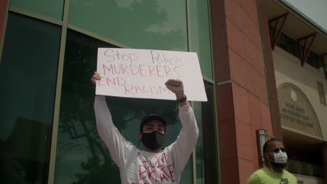Manifestante-Sosteniendo-Un-Cartel-En-La-Protesta-Con-Detener-A-Los-Asesinos-Policiales-Acabar-Con-El-Racismo