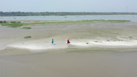 Toma-De-Drones-De-Una-Pareja-Romántica-India-Caminando-En-La-Playa-De-Ganga-Usando-Un-Vestido-Tradicional,-Días-De-Luna-De-Miel