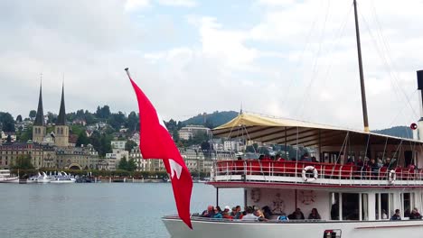 Flag-and-passengers-boat-by-the-lake-in-Lucerne-with-city-and-mountain-in-the-background