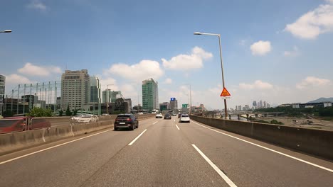 Driver's-POV-Seoul-cityscape,-driving-on-Gangbyeon-Expressway-daytime-near-Han-river-on-sunny-but-cloudy-day