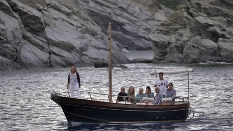 Familie-Auf-Einem-Traditionellen-Boot,-Das-Gemütlich-Im-Meer-Segelt,-Mit-Einer-Küstenklippe-Im-Hintergrund