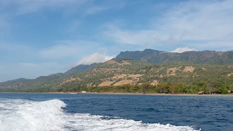 Rugged-tree-covered-coastline-and-blue-sky-of-remote-tropical-island-Atauro-Island-seen-from-the-ocean-with-boat-whitewash-wake