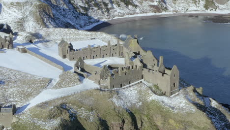 Aerial-view-of-Dunnottar-Castle-ruins-surrounded-by-snow-on-a-sunny-winter-day,-nr-Stonehaven,-Aberdeenshire,-Scotland