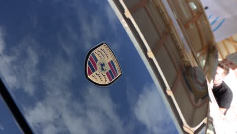 Shiny-luxurious-modern-blue-car-emblem-hood-with-cloudy-sky-reflection,-vertical-medium-shot