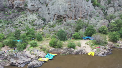 Orbiting-aerial-view:-Camp-site-backed-by-high-cliffs-on-rafting-river