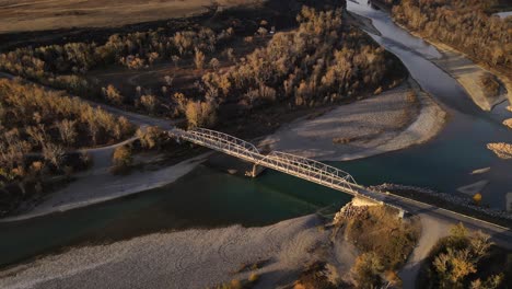 Drone-approaching-an-old-truss-bridge-made-of-steel-near-pincher-creek-in-Alberta,-Canada-during-cold-autumn-sunrise