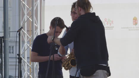 Miembro-Del-Equipo-De-Banda-Arregla-Soporte-De-Micrófono-Para-Saxofonista-Actuando-En-El-Escenario