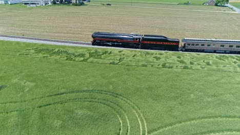 An-Aerial-View-of-a-Steam-Engine-Puffing-Smoke-and-Steam-with-Passenger-Coaches-Traveling-on-a-Single-Track-Fertile-Farmland-and-Countryside-on-a-Beautiful-Cloudless-Spring-Day