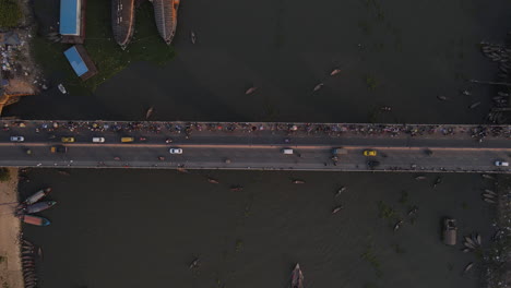 Top-down-view-of-a-bridge-over-a-river-with-cars,-people-and-boats---aerial-drone-ascending-shot