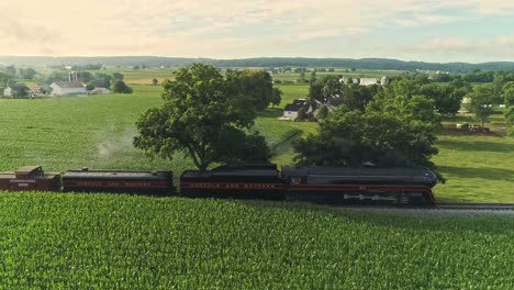 Paisaje-Aéreo-De-Tierras-De-Cultivo-Y-Un-Motor-De-Vapor-Antiguo-Pasa-A-Través-De-Los-Campos-De-Maíz-En-Una-Mañana-De-Verano-Temprano