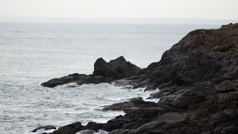 Calm-ocean-waves-crashing-onto-rock-coastline-on-gloomy-overcast-day