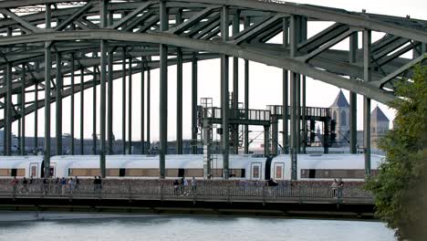 Hohenzollern-bridge-over-the-Rhine-river-near-the-cathedral-with-people-walking-along-the-span-railing,-Locked-medium-shot