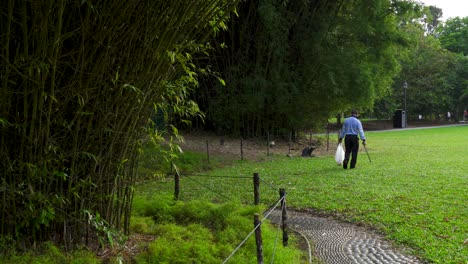 Reiniger-Sammelt-Müll-Aus-Dem-Gras,-Botanischer-Garten-Singapur