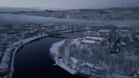 Nidaros-Cathedral-In-Snow-Near-The-Elgeseter-Bridge-Across-River-Nidelva-In-Trondheim,-Norway-During-Winter-Season