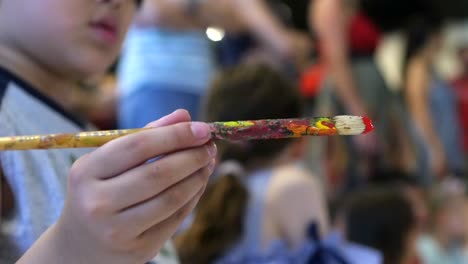 Child-holding-paintbrush-with-small-amount-of-red-paint-on-tip