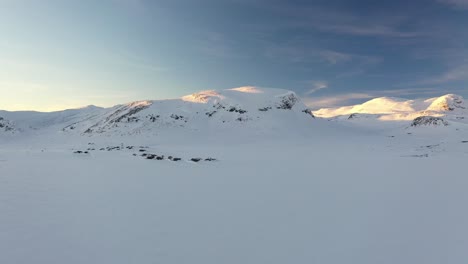 Sonnenuntergang-Winterantenne,-Die-Freizeithütten-In-Der-Nähe-Des-Gefrorenen,-Schneebedeckten-Sees-Eldrevatnet-Und-Den-Sonnenuntergang-Auf-Den-Bergen-Jukleeggi-Und-Ulvehaugnosi-Zeigt