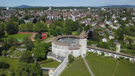 Aerial-orbit-of-Munot-ring-shaped-fort-on-top-of-verdant-hill-in-picturesque-Schaffhausen-village-surrounded-by-trees,-Switzerland
