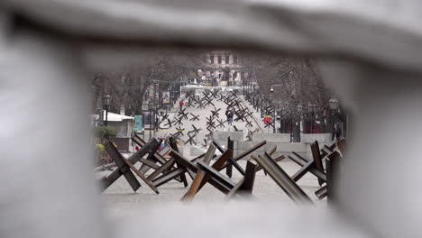 Las-Personas-Que-Pasan-Por-Trampas-De-Tanques-Hechas-De-Vigas-De-Acero-Soldadas-Juntas-Se-Ven-A-Través-De-Un-Agujero-De-Francotirador-En-Una-Barricada-De-Carretera-De-Sacos-De-Arena-Durante-La-Invasión-Rusa-De-Ucrania