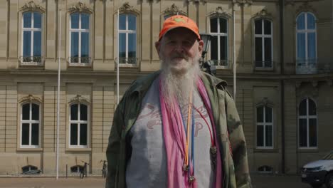 Warmhearted-elderly-man-in-front-of-downtown-Stuttgart-Parliament-building-at-noon,-Germany,-Europe,-panning-view-angle