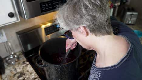 Stirring-raspberries-and-blueberries-in-a-large-pot-to-make-homemade-jam---over-the-shoulder-view