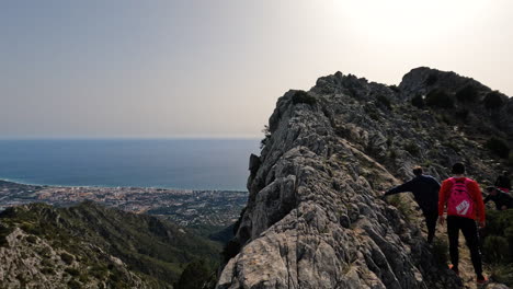 4k-Shot-of-two-hikers-walking-on-a-slim-mountain-ridge-at-La-Concha,-Marbella,-Spain